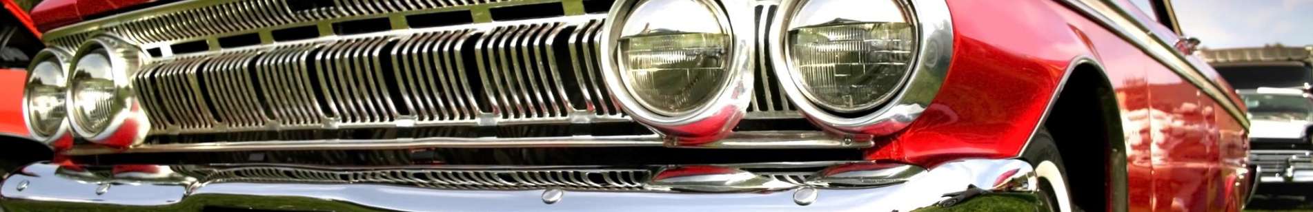 Shiny chrome bumper and headlight of a classic red muscle car.