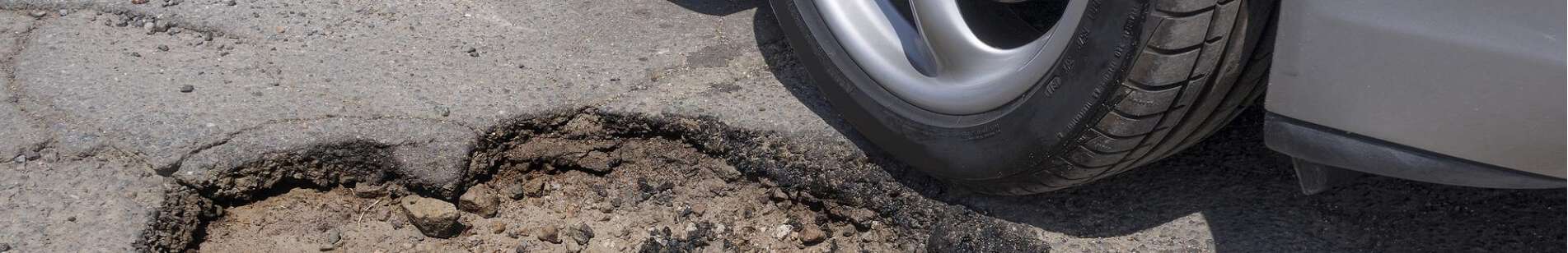 A car drives around a pothole on the road.