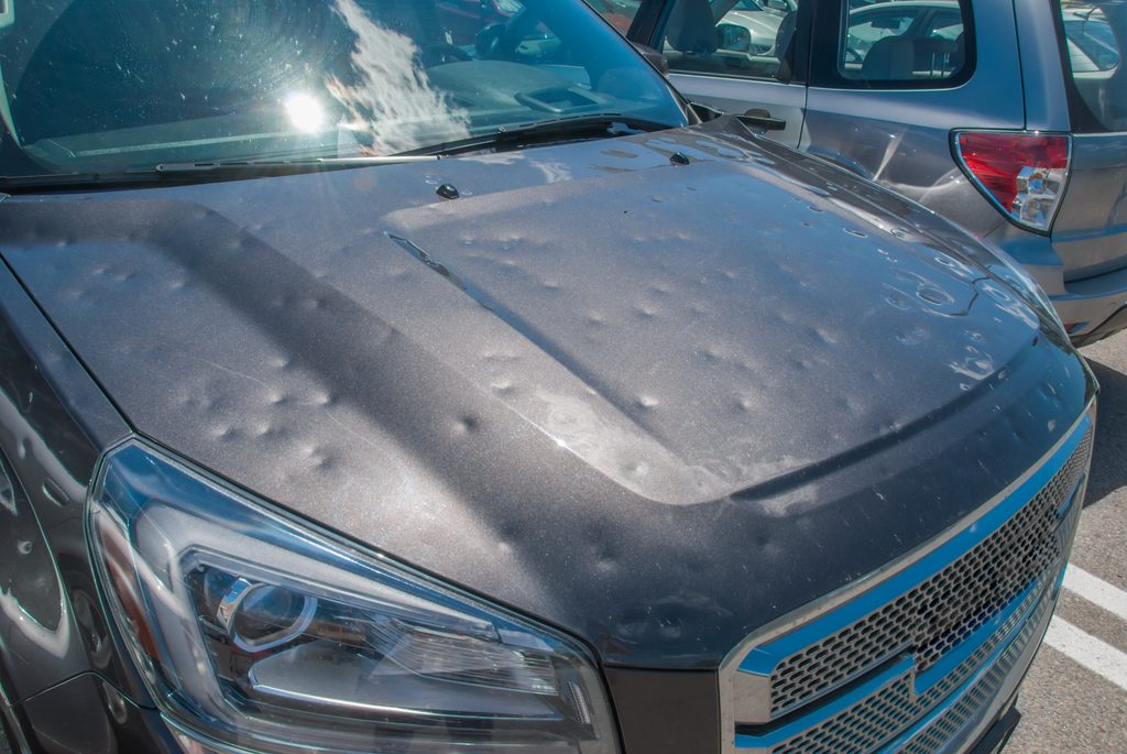 does car insurance cover hail damage? coverage and claims for pa drivers a dark gray car with a hood covered in multiple dents from hail damage, raising questions about whether car insurance covers hail damage.